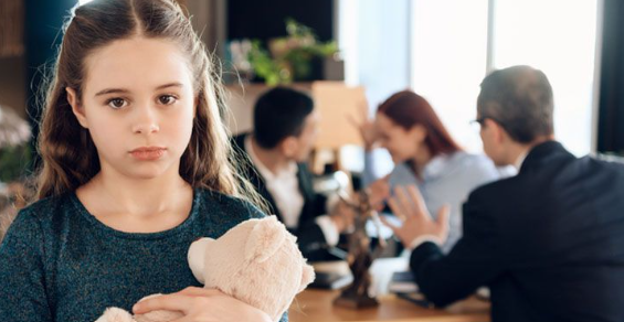 Girl holding toy bear in front of child custody lawyer in a meeting with parents